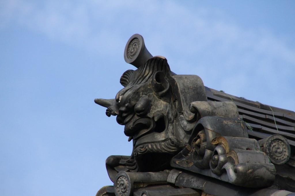 A weathered demon-faced onigawara ridge-end tile on a temple roof at Myoshin-ji in Kyoto, against a blue sky